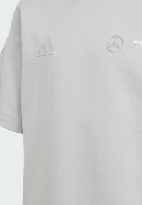 Camiseta de algodón gris claro con logotipos en relieve de Adidas y Mercedes. Mangas cortas con una textura suave para mayor comodidad.