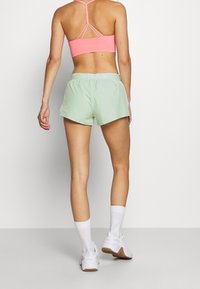 Pantalones cortos deportivos verde menta con cintura elástica, combinados con un sujetador deportivo rosa que presenta un diseño de espaldas con tiras.
