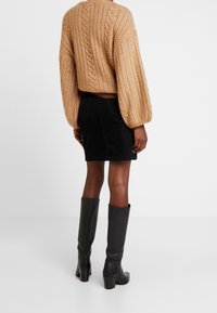 Chunky gebreide beige trui met een cropped fit, gecombineerd met een zwarte corduroy rok en zwarte laarzen met hak tot de knie.