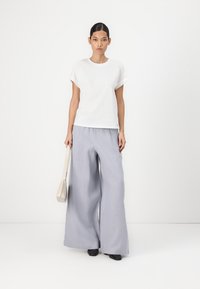Hvit oversized t-skjorte med korte ermer kombinert med lysegrå vide bukser. Modellen bærer en liten beige håndveske og har på seg svarte sko.