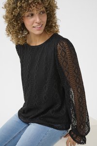 Black long-sleeve lace top with diamond patterns, sheer sleeves, and a round neckline, paired with blue jeans. Textured fabric provides contrast.