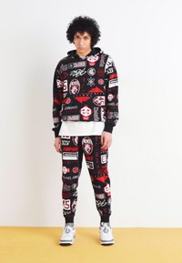 Completo felpa con cappuccio e pantaloni neri, con grafiche vivaci a tema sportivo in rosso e bianco. Realizzato in tessuto morbido con polsini a costine.