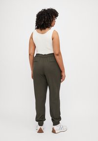 Joggers verde oliva con cintura y puños elásticos, que cuentan con dos bolsillos traseros. Combinados con una camiseta sin mangas blanca y zapatillas blancas.