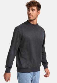Mørkegrå sweatshirt med en glat tekstur, rund halsudskæring og ribbede manchetter. Modellen bærer lyseblå jeans, hvilket giver et afslappet udtryk.