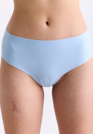 Die Körpermitte einer Frau, die nahtlose, hellblaue Unterwäsche trägt, zeigt Haut und einen kleinen Muttermal am oberen linken Oberschenkel.