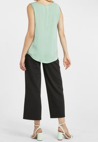 Blusa sin mangas de color verde menta con un dobladillo redondeado, combinada con pantalones anchos negros y sandalias de tacón verde menta. Textura de tela suave.