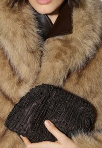 Brun pelsimitation-frakke med en bred krave, kombineret med en mørk stofclutch med teksturerede perler og plisseret design.