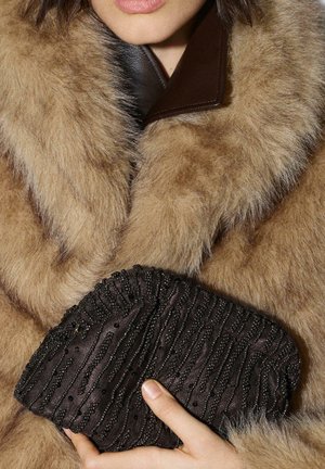 Bruine jas van namaakbont met een brede kraag, gecombineerd met een donker stoffen clutch met een gestructureerd kralenwerk en geplooid ontwerp.
