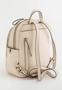 Mochila de cuero crema con herrajes dorados, forma estructurada, doble cremallera y acentos negros. Correderas ajustables y bolsillo lateral visible.