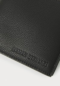 Čierna peňaženka vyrobená z textúrovanej kože, s embosovaným brandingom "ARMANI EXCHANGE" v modernom písme. Čisté hrany a minimalisticý dizajn.