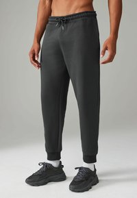 Donkergrijze joggingbroek met een elastische tailleband, een trekkoord, zijzakken en taps toelopende boorden. Gemaakt van een zachte, gladde stof.