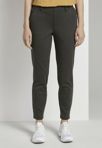 Donkergrijze taps toelopende broek met elastische tailleband, zijzakken en een gladde textuur. Gecombineerd met witte sportschoenen.