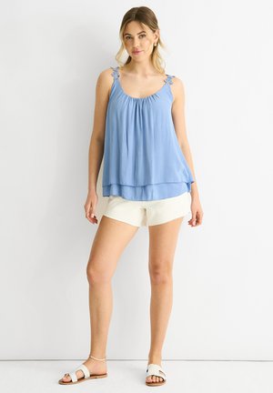 Lyseblå ærmeløs top med samlede halsudskæring og blomstrede detaljer på stropperne, parret med hvide shorts. Glat stof, afslappet pasform.