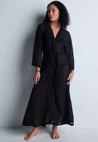 Robe noire longue en style kimono, transparente, avec un design enveloppant, une taille à nouer et des manches longues. Texture lisse, longueur jusqu'aux chevilles, style minimaliste.