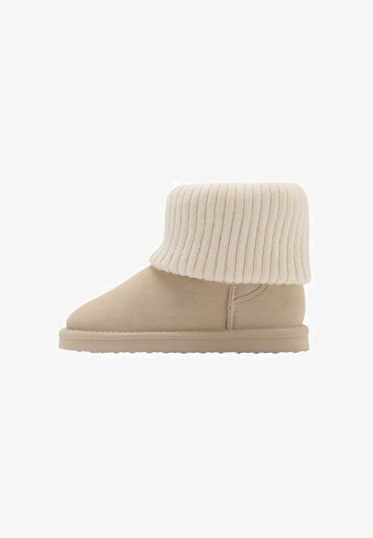 Beige enkellaarsjes met een zachte suède buitenkant en een dikke, geribbelde crèmekleurige gebreide manchette. De zool is plat en heeft een textuur voor grip.