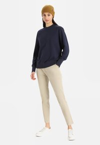 Navy crewneck sweatshirt, beige slim-fit pants, and white sneakers; styled with a mustard ribbed beanie, offering a casual look.