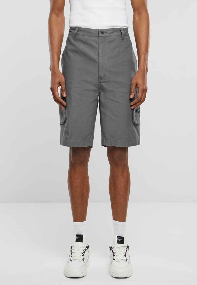 Shorts cargo gris fabriqués en tissu léger, avec des poches latérales et une coupe classique, portés par un mannequin portant des baskets blanches.