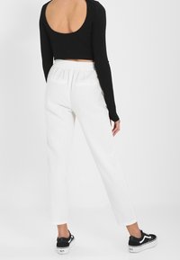 Pantalons blancs amples avec une taille élastique, associés à un crop top noir à manches longues, vus de derrière. Tissu texturé, style décontracté.