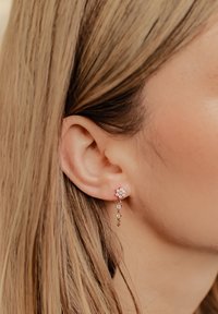 Ohrringe mit Goldfinish, die ein Blütenmuster zeigen, verziert mit klaren Rhinestones und herabhängenden Kettenakzenten.