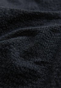 Textureeritud tume sinine kangas väikeste, tõstetud mustritega. Pehme, kootud tekstuur loob nähtavad voldid ja kihid.