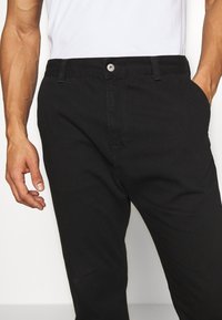 Černé bavlněné kalhoty slim fit, se zipem, předními kapsami a stříbrným knoflíkem. Hladká textilie a jednobarevný design.