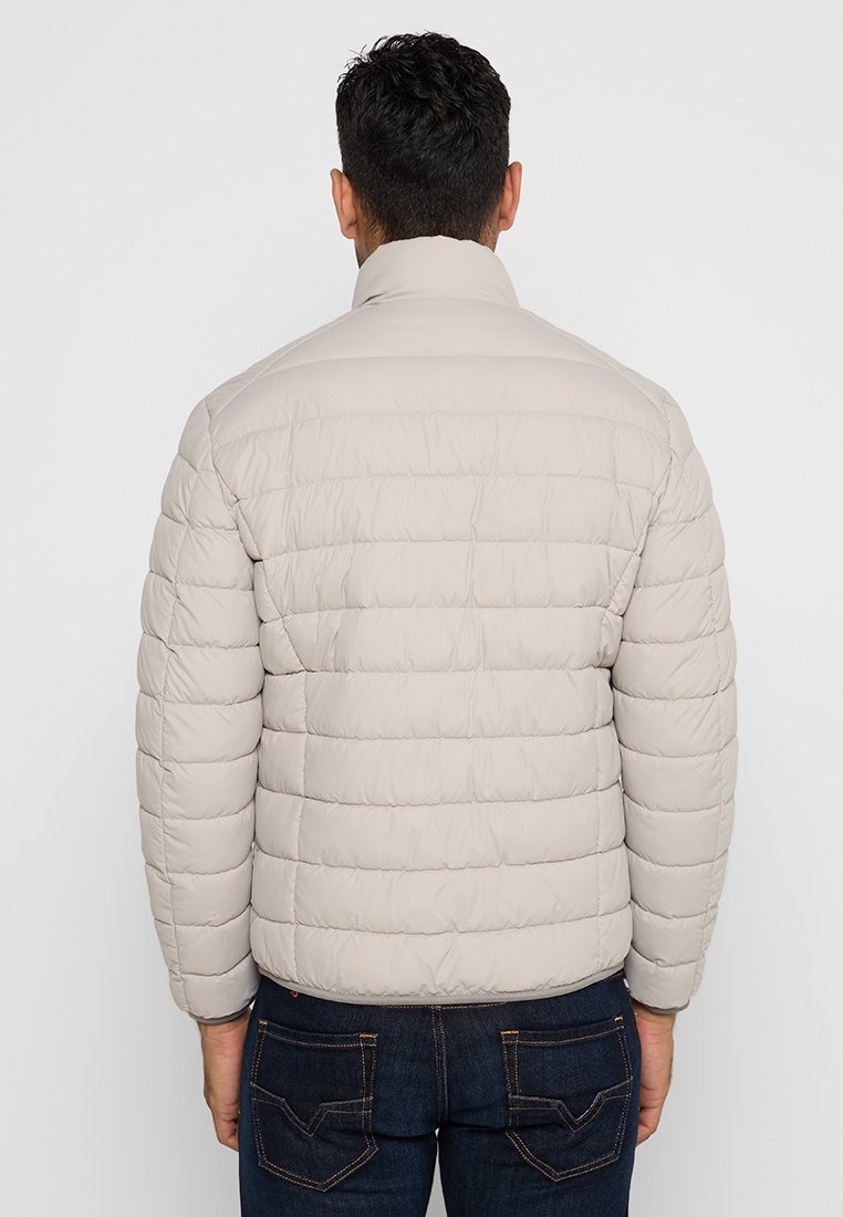 Helle beige Steppjacke mit gestepptem Muster, hohem Kragen und taillierter Passform. Sichtbare Nähte und elastische Bündchen.