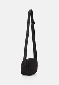 Borsa a tracolla nera con forma rettangolare, dotata di chiusura con zip e tracolla regolabile con il logo "TOMMY JEANS" in grigio.