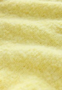 Teksturowana żółta tkanina o miękkim, puszystym wyglądzie. Powierzchnia ma jasny, nierówny wzór, co wskazuje na przytulny, ciepły materiał.