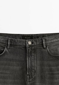 Jeans neri in denim a vestibilità affusolata con bottone argento, passanti per cintura e tasche anteriori. Il tessuto ha una texture liscia con sottili motivi intrecciati.