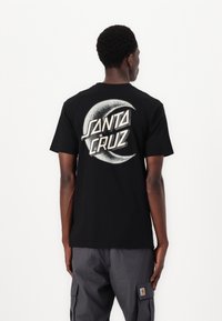 Schwarzes Baumwoll-T-Shirt mit einem großen weißen und silbernen Grafikdesign mit "SANTA CRUZ" und einem Halbmond auf der Rückseite. Normale Passform.