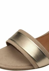 Sandale glissière beige avec une large sangle métallique dorée et une texture semblable à du daim. Caractérisée par un design ouvert à l'avant et plat pour un enfilage facile.