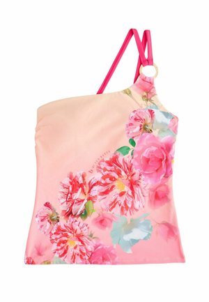 Frau mit schulterlangem Haar, die einen geblümten Ein-Schulter-Badeanzug trägt, vor einer Steinmauer mit rosa Blumen in der Nähe.