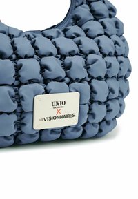 Borsa blu a forma di cuscino realizzata in tessuto testurizzato, con forme arrotondate e un'etichetta del logo distintivo recante la scritta "UNIO Hamburg x LES VISIONNAIRES."