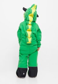 Groene gewatteerde romper met gele accenten, een dinosaurustail, en zwarte oordetails. Voorzien van een rits aan de voorkant en brede zwarte manchetten bij de enkels.