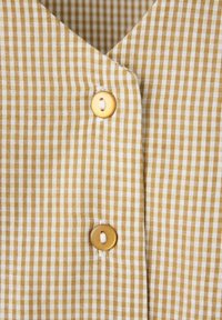Tissu à carreaux jaune et blanc avec deux boutons ronds marron clair cousus verticalement le long du pli central.