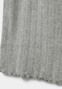 Sivi pleteni materijal s vertikalnim rebrima i valovitim rubom. Sadrži teksturirani uzorak s malim dijamantskim oblicima.