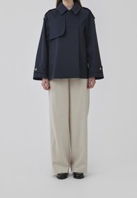 Navy cropped jacket with a wide collar, large pockets, and buttoned cuffs, paired with light beige wide-leg trousers and black footwear.