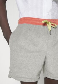 Pantalones cortos de rizo gris con una cinturilla elástica naranja y un cordón verde lima. Cuenta con bolsillos laterales y una textura suave.