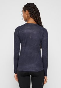 Długi rękaw top sportowy w ciemnonawym materiale, z teksturowanym wykończeniem, raglanowymi rękawami oraz odblaskowym pionowym paskiem na plecach.