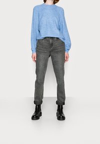 Suéter texturizado azul claro con mangas largas, combinado con unos pantalones de mezclilla grises de cintura alta, arremangados, y botas negras hasta el tobillo.