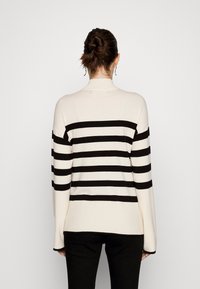 Maglione lavorato a maglia con righe orizzontali nere su sfondo crema, con collo alto, maniche lunghe e vestibilità comoda.