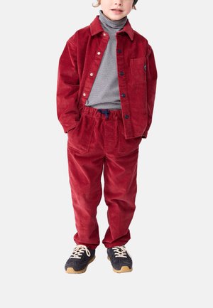 Rote Cordjacke und passende Hose, kombiniert mit einem gestreiften Rollkragenpulli. Enthält schwarze Schuhe mit hellen Sohlen und eine Tasche an der Jacke.