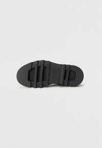 Suola di scarpa nera in materiale gommoso testurizzato, con diverse scanalature orizzontali e una punta arrotondata. Finitura liscia senza marchi visibili.