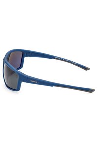 Gafas de sol azules con acabado mate, diseño envolvente, lentes grises y logotipo "Timberland" plateado a lo largo de la patilla, montura de plástico liviana.