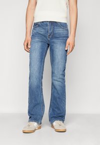 Lys blå denimjeans med rett benpassform, med kontraststing og femlommers design, kombinert med beige joggesko.