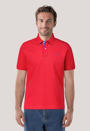 Rotes Poloshirt mit einem Kragen mit blauen Akzenten, aus Baumwollstoff gefertigt. Enthält das GANT-Logo in Blau auf der Brust.