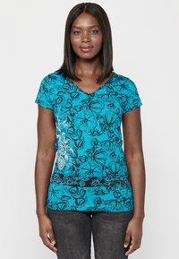 T-shirt teal à fleurs avec des manches courtes et un col en V, présentant des contours noirs de fleurs et une bande inférieure noire contrastante.