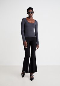 Gray long-sleeve top with a scoop neckline, paired with black flared pants. Model wears black sunglasses and heeled shoes with buckle accents.