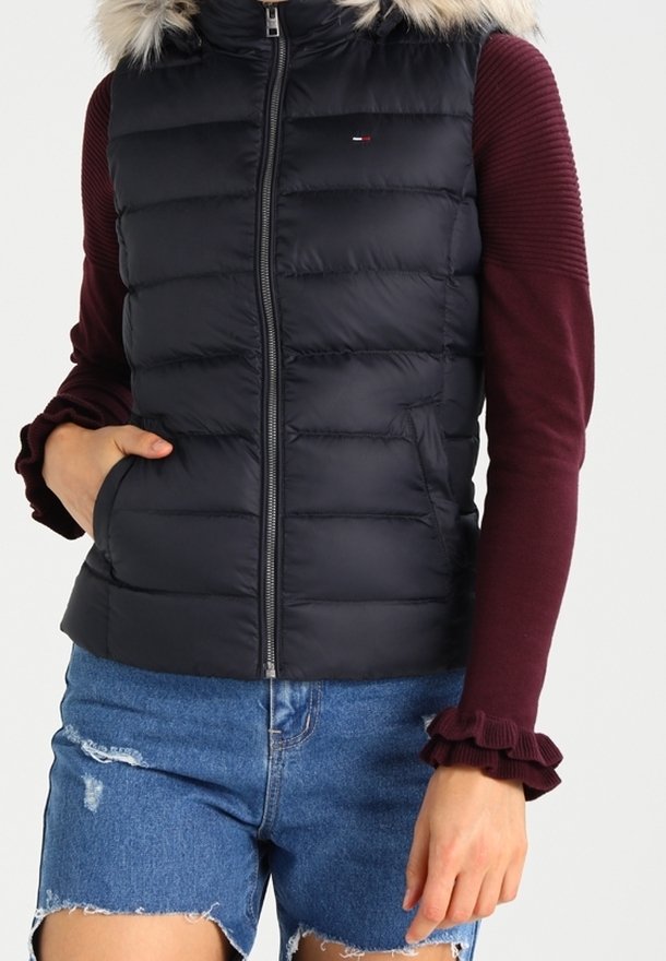 Vadderad väst med svart yta och vinröda stickade ärmar, med en fuskpäls-huva, dragkedjestängning och volangärmar.