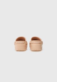 Sabots Crocs beige clair en matériau flexible, avec une sangle au dos et des semelles texturées. Présente un design minimaliste sans motifs supplémentaires.